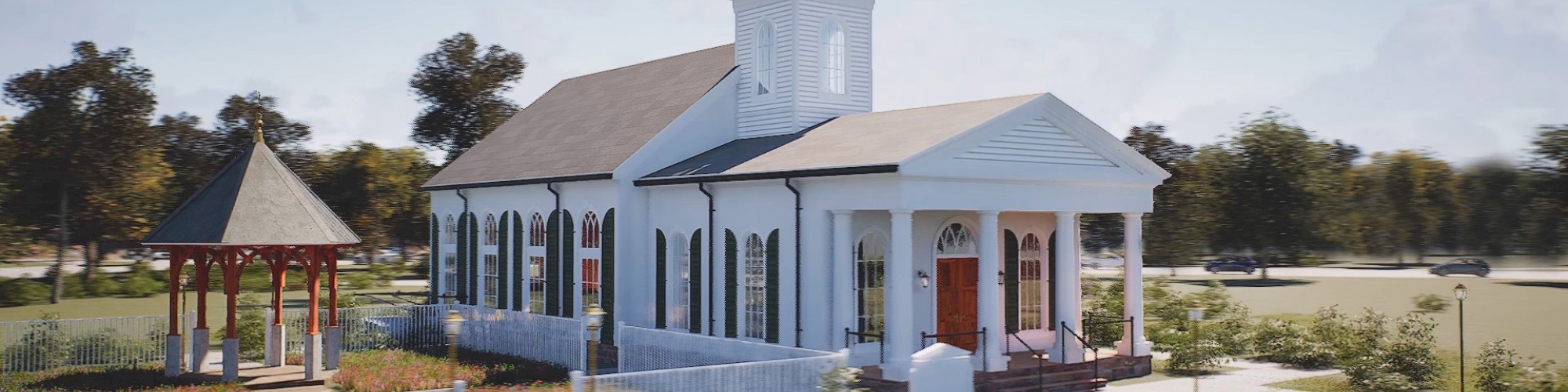 A small white church with a steeple, a red door, and arched windows, surrounded by greenery and a white fence, with a gazebo nearby.