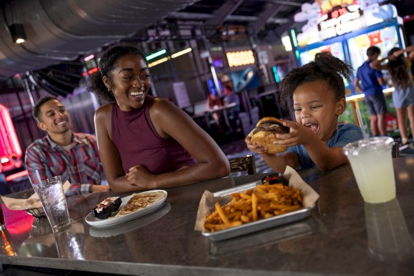 A family is enjoying a meal at a restaurant with burgers, fries, and drinks. The atmosphere appears lively and engaging.